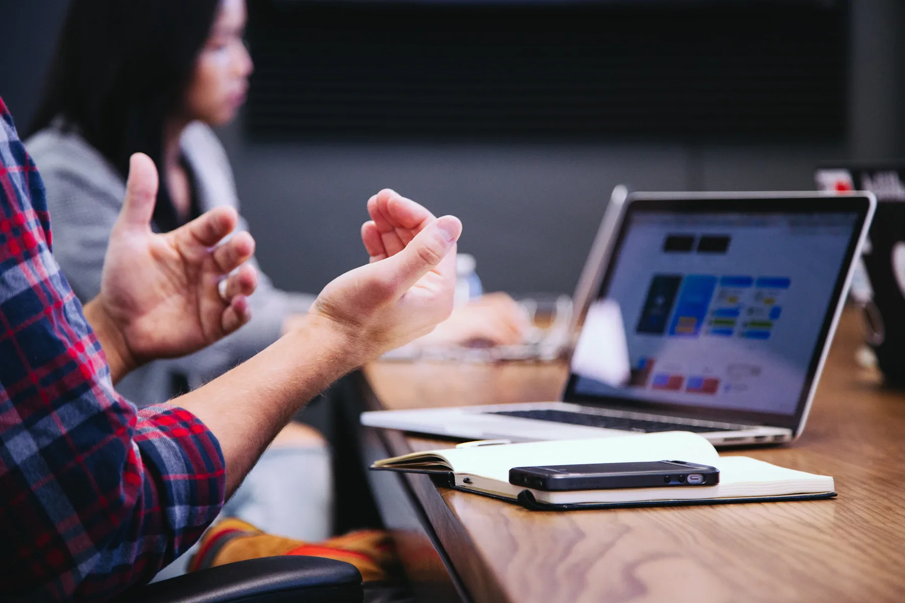 A discussion around a table with a laptop, handwritten notes and a person gesturing.
