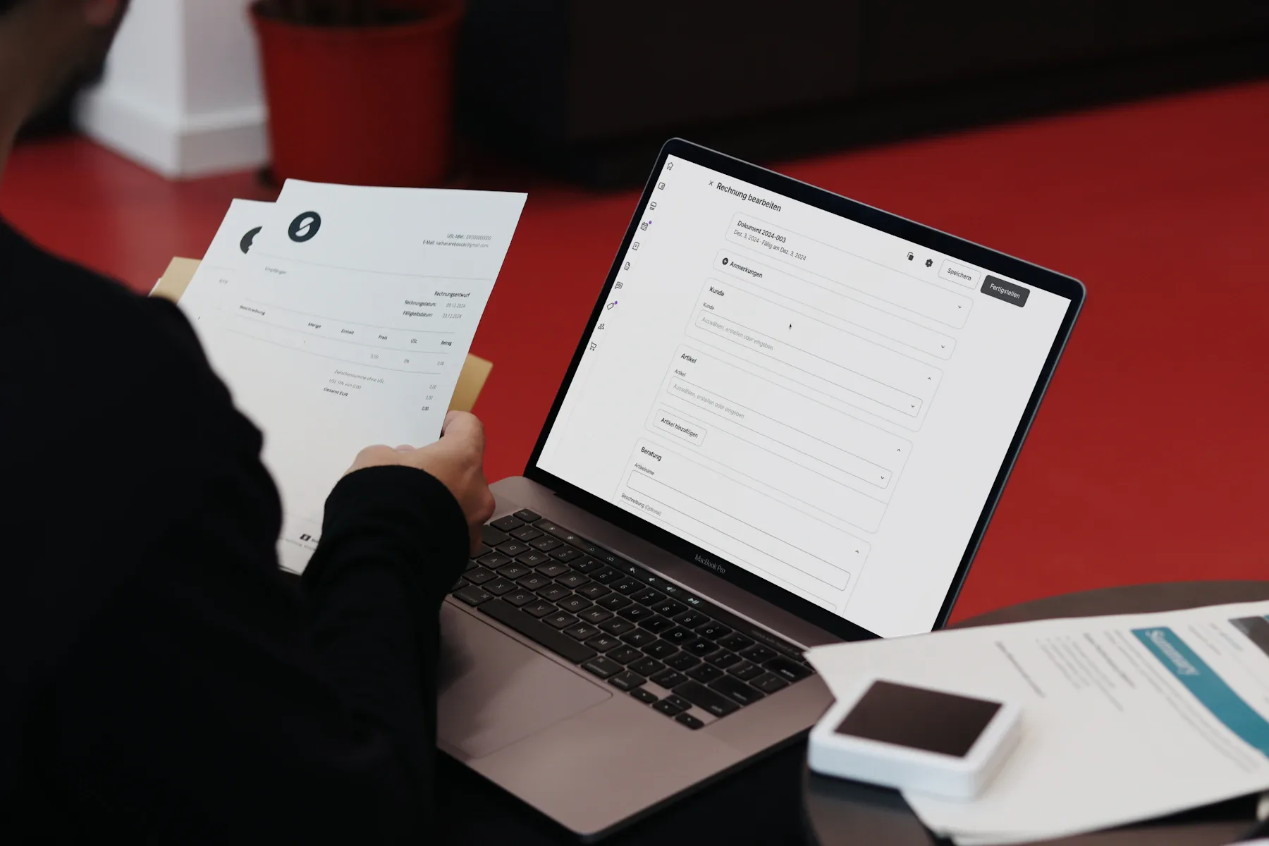 A person holding invoice paperwork beside a laptop displaying invoicing software.